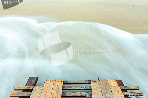 Image of Waves roll onto a sandy beach, bottom part of a wooden bridge, long exposure