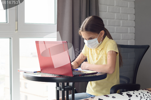 Image of A girl in a medical mask learns remotely at home via the Internet