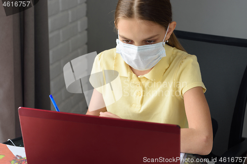 Image of Girl in medical mask studies online at home