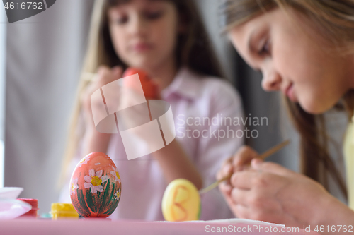 Image of Children paint Easter eggs, focus on the egg in front of them