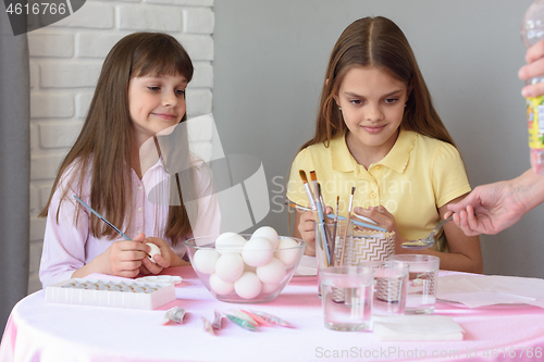 Image of Mom prepares a solution for painting eggs, children are watching with curiosity