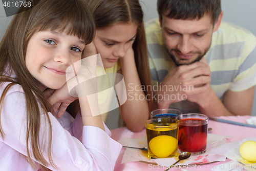 Image of The family waits until the eggs are painted in a glass with dyes, the girl cheerfully looked into the frame