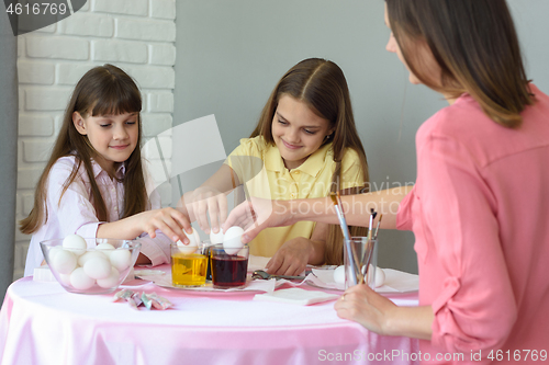 Image of Children and mom dip chicken eggs in a dye solution