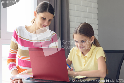 Image of A girl and a girl are sitting at a table and browsing web pages in a laptop