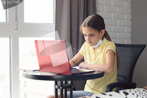 Image of Pensive child sitting at the table taking off a medical mask and doing homework