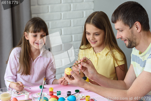 Image of Dad shows children how to easily and easily paint Easter eggs