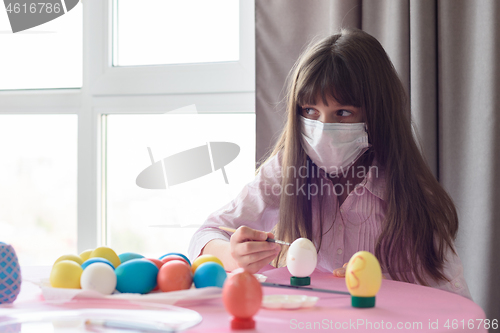 Image of The sick girl alone paints Easter eggs for the holiday