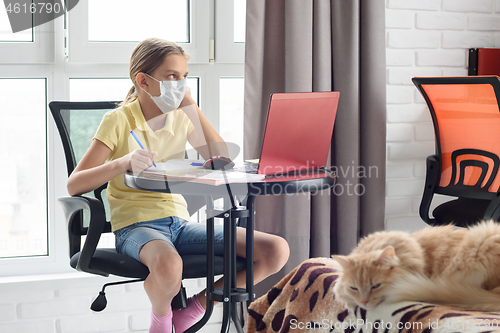 Image of A sick girl in self-isolation sits at a table and does homework online