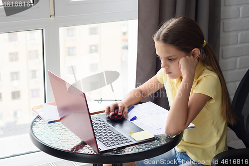 Image of Girl thoughtfully doing homework, sitting at a table by the window