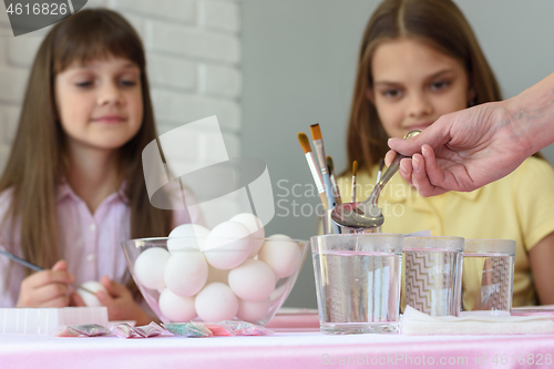 Image of Mom pours vinegar in glasses of water for coloring eggs for Easter holidays