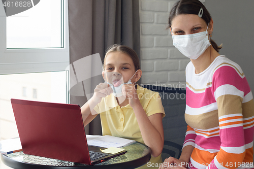 Image of The girl took off her medical mask and showed her tongue, doing homework in self-isolation mode