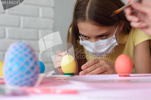 Image of Close-up of a girl in a medical mask who paints Easter eggs