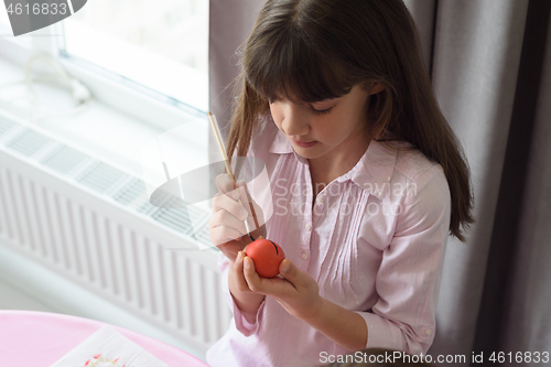 Image of Girl paints an easter egg sitting by the window in a home environment