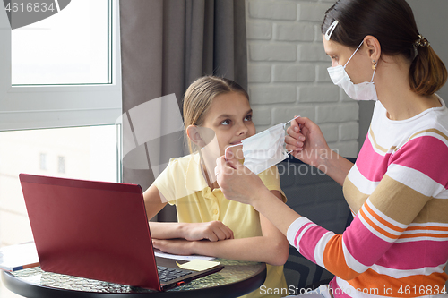 Image of Girl at home puts on protective medical mask to child