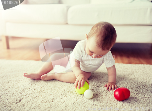 Image of happy baby playing with balls on floor at home