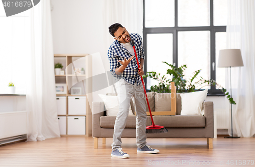 Image of man with broom cleaning and singing at home