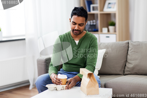 Image of indian man with takeaway coffee and food at home