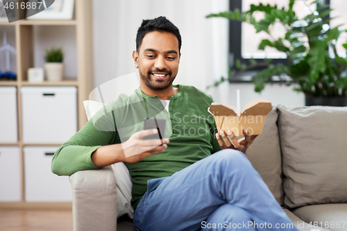 Image of smiling indian man eating takeaway food at home