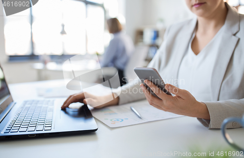 Image of businesswoman with smartphone and laptop at office