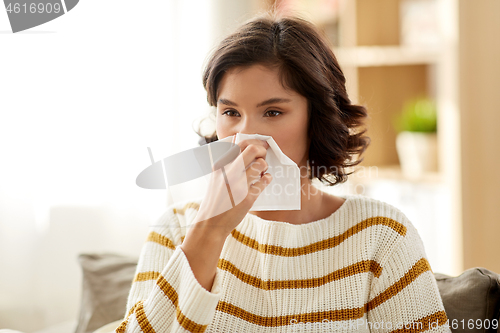 Image of sick woman blowing nose in paper tissue at home