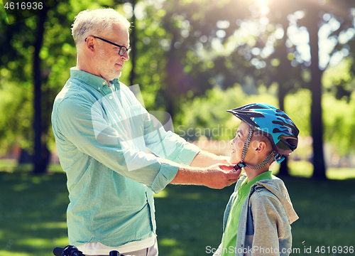 Image of old man helping boy with bike helmet at park