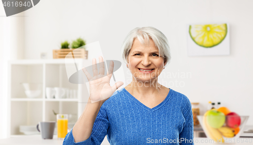 Image of smiling senior woman showing her palm in kitchen