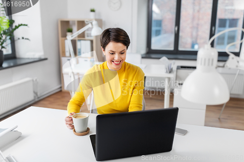 Image of businesswoman with laptop drinks coffee at office