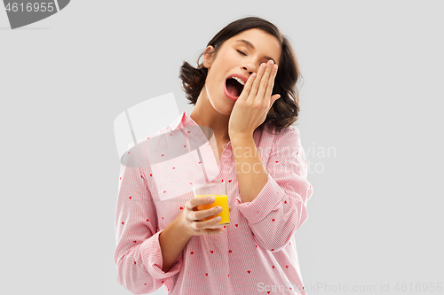 Image of happy yawning young woman in pajama with juice