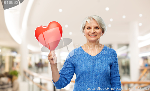 Image of smiling senior woman with red heart shaped balloon