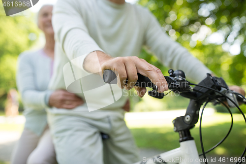 Image of happy senior couple riding one bicycle at park
