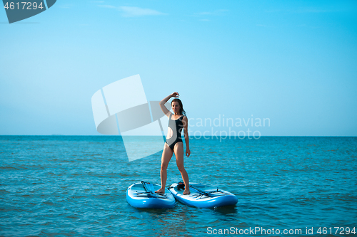 Image of Happy beautiful young girl with paddle board on beach. Blue sea in the background. Summer vacation concept.