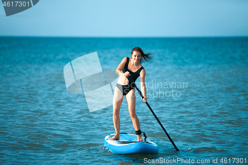 Image of Happy beautiful young girl with paddle board on beach. Blue sea in the background. Summer vacation concept.