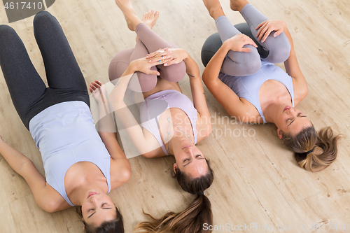 Image of Group of three young sporty attractive women in yoga studio, lying on the floor, stretching and relaxing after the workout. Healthy active lifestyle, working out indoors in gym