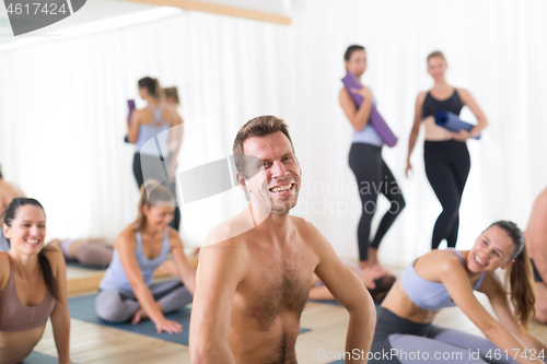 Image of Portrait of a cheerful male hot yoga instructor relaxing after giving yoga class to large group of sporty attractive people. Healthy active lifestyle, working out indoors in gym.