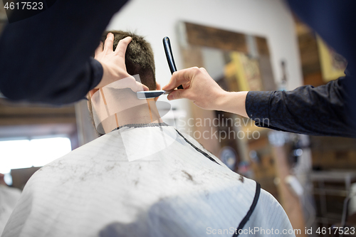 Image of man and barber with straight razor shaving hair