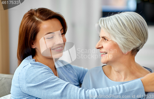 Image of senior mother with adult daughter hugging at home