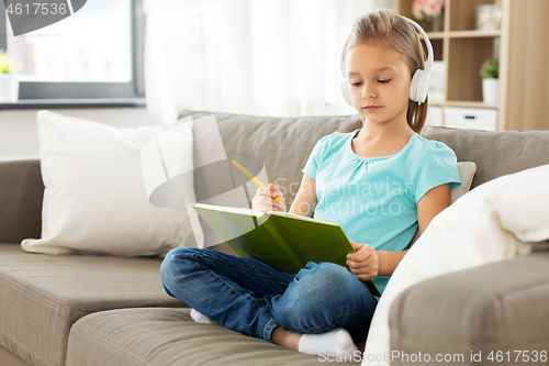 Image of girl in headphones with diary on sofa at home
