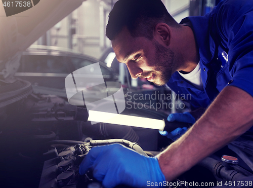 Image of mechanic man with lamp repairing car at workshop