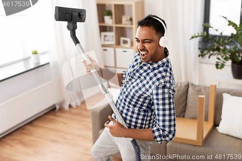 Image of man in headphones with vacuum cleaner at home