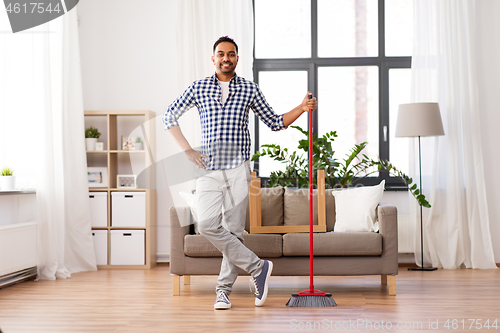 Image of smiling indian man with broom cleaning at home