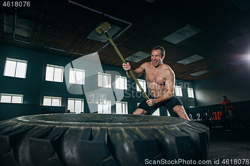 Image of Shirtless man flipping heavy tire at gym