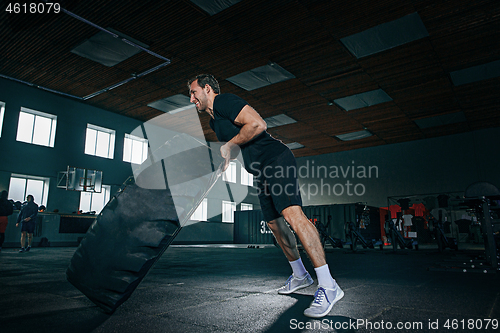 Image of Shirtless man flipping heavy tire at gym