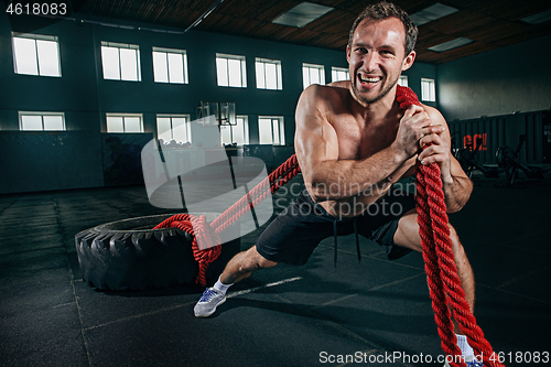 Image of Shirtless man flipping heavy tire at gym