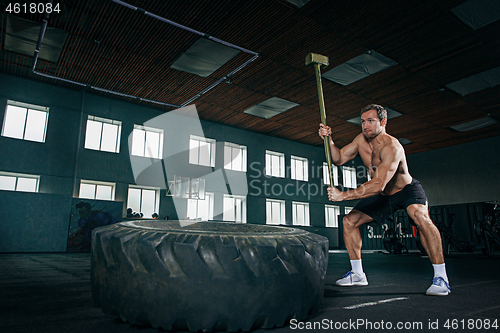 Image of Shirtless man flipping heavy tire at gym