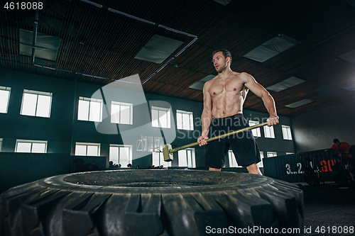 Image of Shirtless man flipping heavy tire at gym