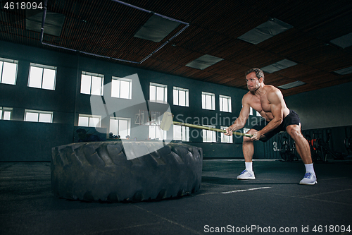 Image of Shirtless man flipping heavy tire at gym