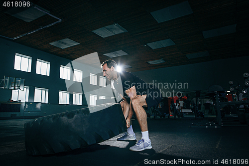 Image of Shirtless man flipping heavy tire at gym