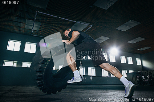 Image of Shirtless man flipping heavy tire at gym