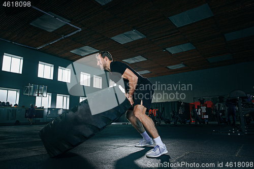 Image of Shirtless man flipping heavy tire at gym