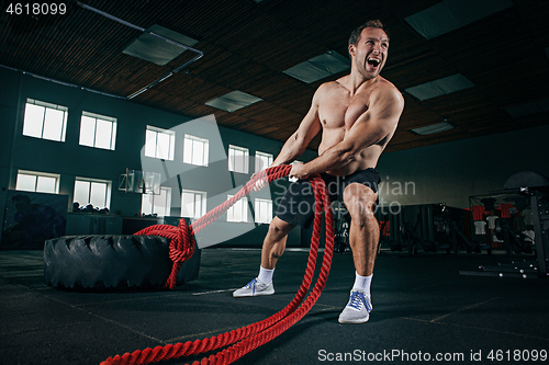 Image of Shirtless man flipping heavy tire at gym